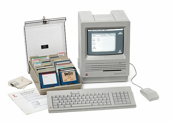 Macintosh Computer aus den 80ern mit Tastatur, Maus und Floppy-Disk-Behälter